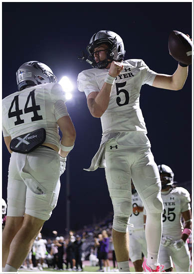 Two people in white football uniforms and helmets are on a field at night, with one holding a football in a throwing position. Description generated by AI