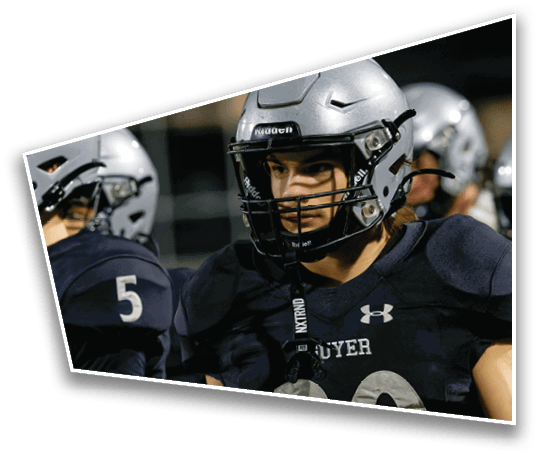 Two people wearing football helmets and dark jerseys with numbers are standing close together on a field. Description generated by AI