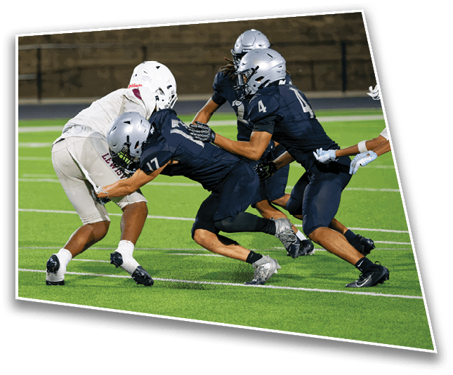 Two people in football uniforms are engaged in a tackle on a green field during a game. Description generated by AI