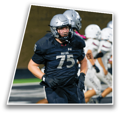 A person wearing a dark football uniform with the number 75 and a silver helmet is running on a football field with other players in the background. Description generated by AI