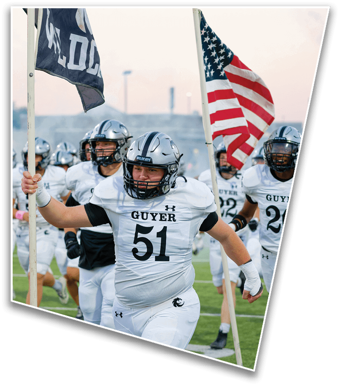 People in football uniforms are running on a field with one person holding a flag and leading the group. Description generated by AI