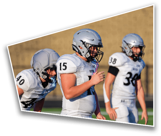 Three people wearing white football uniforms and helmets stand on a field with a blurred background. Description generated by AI
