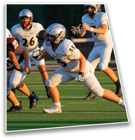 People in football uniforms are actively engaged in a game on a green field with one player in a crouched stance and another preparing to throw a football. Description generated by AI