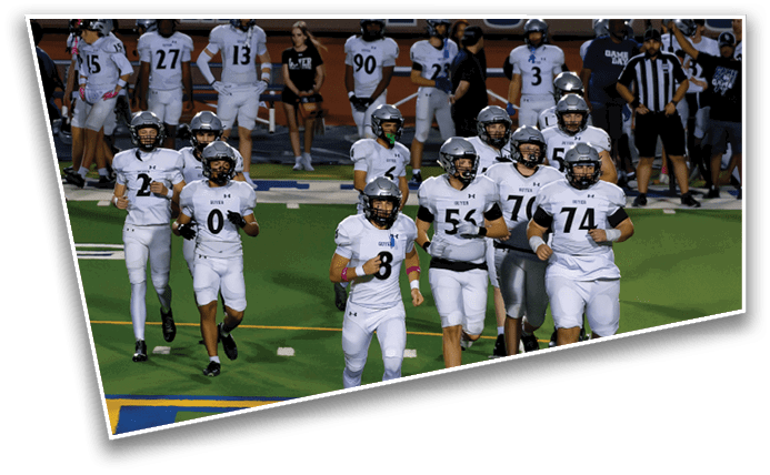 A group of people in white football uniforms with helmets are running on a green field. Description generated by AI