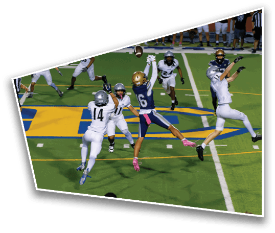 A group of people playing football on a field with one person in a blue uniform and pink gloves jumping to catch the ball while others in white uniforms attempt to block. Description generated by AI
