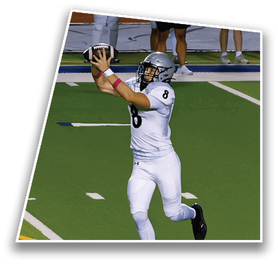A person wearing a football helmet and uniform is catching a football on a field with other people standing in the background. Description generated by AI