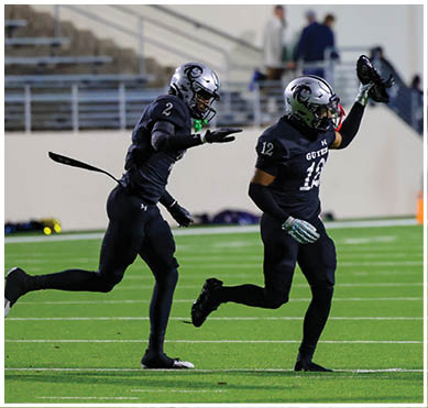 Three people in black football uniforms and helmets are running on a green field with empty bleachers in the background. Description generated by AI