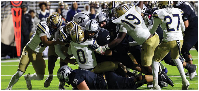Several football players in uniforms are engaged in a tackle on a green field during a game. Description generated by AI