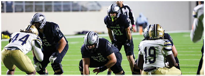 Several people in football uniforms are positioned on a field preparing for a play during a game. Description generated by AI