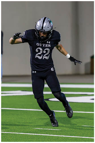 A person wearing black shoes is running on a green sports field with white boundary lines. Description generated by AI