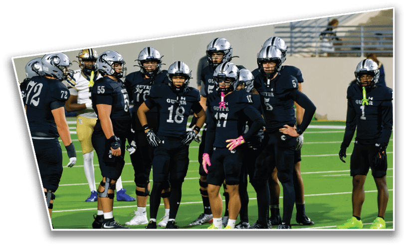 A group of people wearing black football uniforms and helmets are standing together on a green football field. Description generated by AI