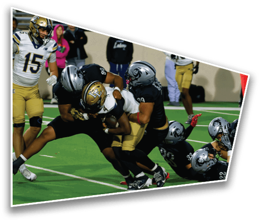 Several people in football uniforms are engaged in a tackle on a green field while others stand nearby watching. Description generated by AI