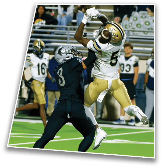 Two football players in action on a field with one player in white and gold uniform jumping to catch the ball while being closely defended by a player in a dark uniform. Description generated by AI