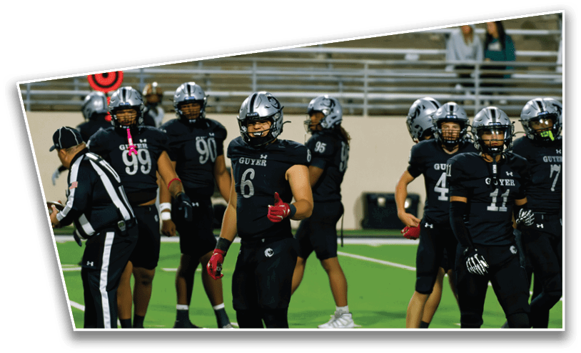 A group of football players in black uniforms and helmets stand on a field with one player giving a thumbs-up while a referee holds a football nearby. Description generated by AI
