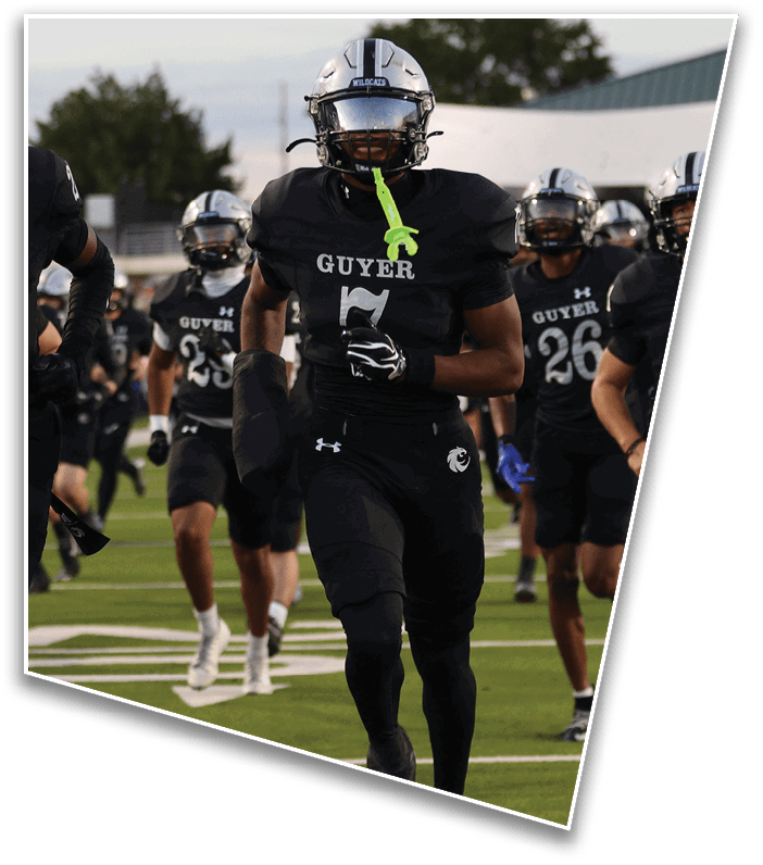 People wearing black football uniforms with “GUYER" on the jerseys are running on a football field during a game or practice. Description generated by AI