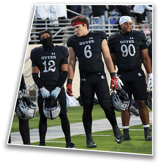 Four football players in black Guyer uniforms stand on the field with a crowd in the background. Description generated by AI