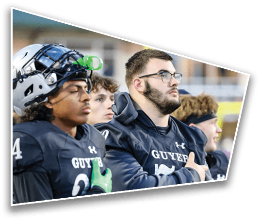 Three people wearing dark sports uniforms are sitting closely together, with one person wearing a helmet and another wearing glasses, appearing focused and attentive. Description generated by AI