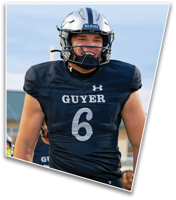 A person wearing a black football uniform with the word “GUYER" and the number 6 on the front is smiling while standing outdoors. Description generated by AI