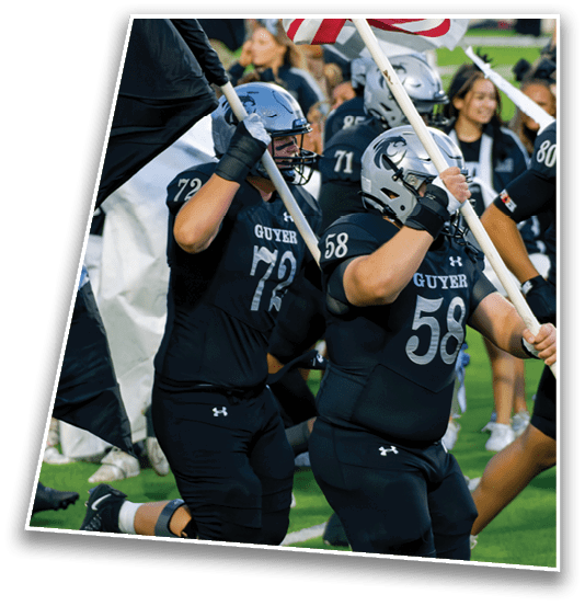 People in football uniforms are running on a field with one person holding a large flag. Description generated by AI