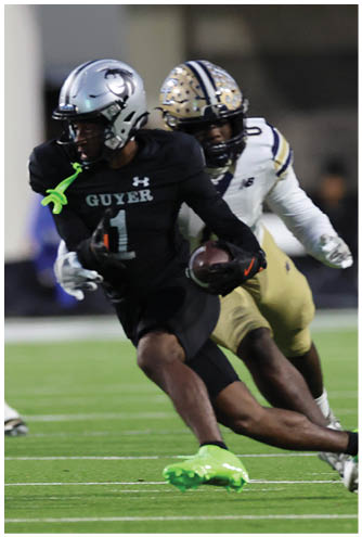Two people wearing football helmets and black uniforms are on a field with a blurred background. Description generated by AI