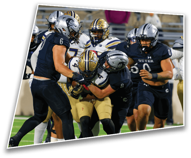 Several football players in black and gold uniforms are engaged in a tackle on a green field during a game. Description generated by AI