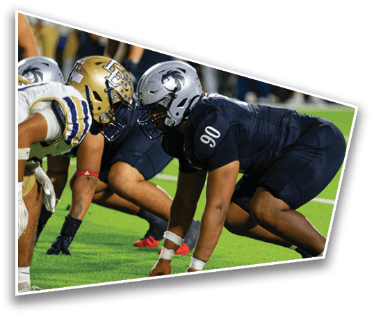 Two football players in helmets and uniforms are crouched facing each other on a green field, ready for a play. Description generated by AI