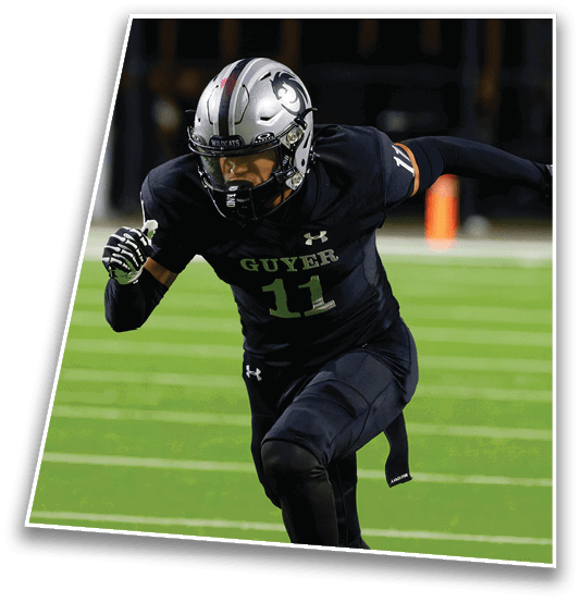 A person wearing a silver football helmet and black jersey with “GUYER" on the front is leaning forward on a football field with a blurred background. Description generated by AI