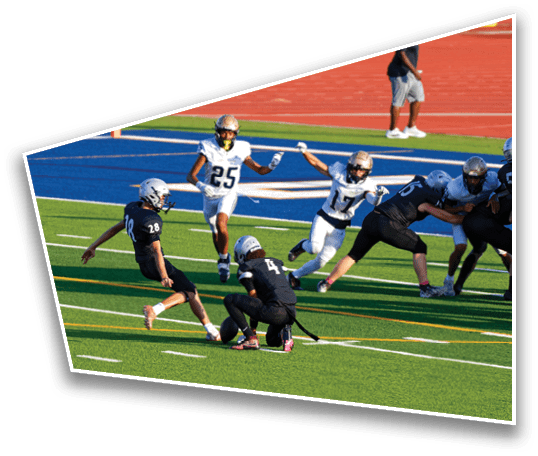 Several people in football uniforms are actively playing on a green field with a blue and red track in the background. Description generated by AI