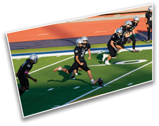 A group of people in black sports uniforms and helmets are on a football field with one person kicking a football while others prepare to run. Description generated by AI