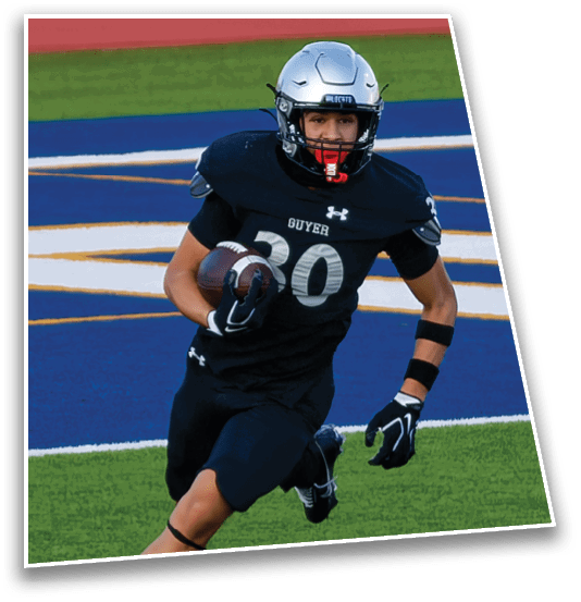A person wearing a silver football helmet and black uniform is on a field with green grass and a red running track in the background. Description generated by AI