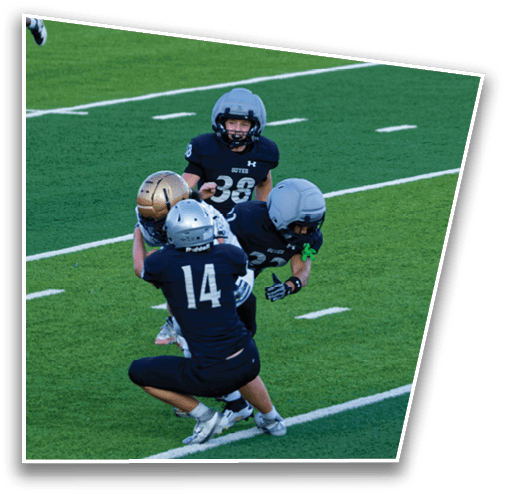 Four people wearing football helmets and uniforms are engaged in a play on a green football field with white yard lines. Description generated by AI