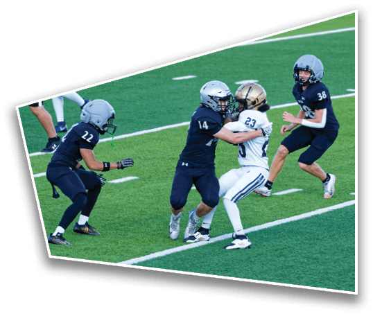 Four people wearing football helmets and uniforms are engaged in a play on a green field with white yard lines. Description generated by AI