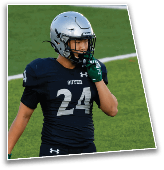 A person wearing a football uniform with the number 24 and a silver helmet is standing on a green field, touching their faceguard. Description generated by AI