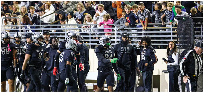 A group of football players and coaches in black uniforms are walking on the sidelines of a stadium with a crowd of spectators in the background. Description generated by AI
