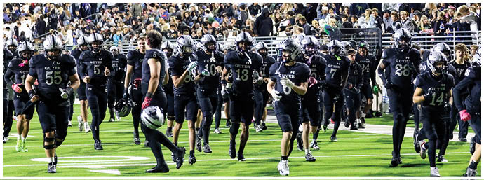 A group of people wearing black football uniforms and helmets are walking on a green field with a crowd in the background. Description generated by AI