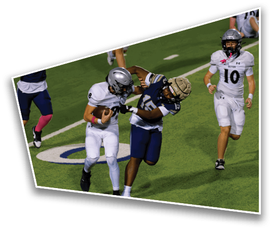 Two people in football uniforms are engaged in a tackle on a green field during a game. Description generated by AI
