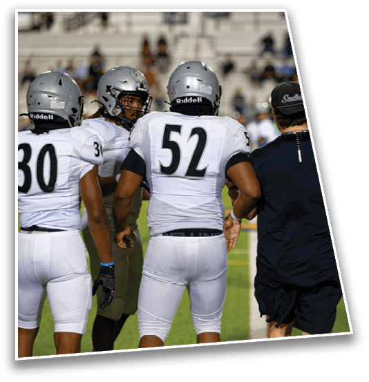 A person wearing a white football uniform with the number 52 is walking arm-in-arm with another person dressed in dark athletic clothing and a cap on a football field. Description generated by AI