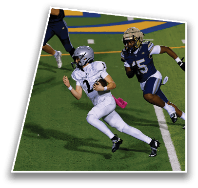 A person in white football gear is running with the ball while being chased by a person in dark blue football gear on a green field. Description generated by AI