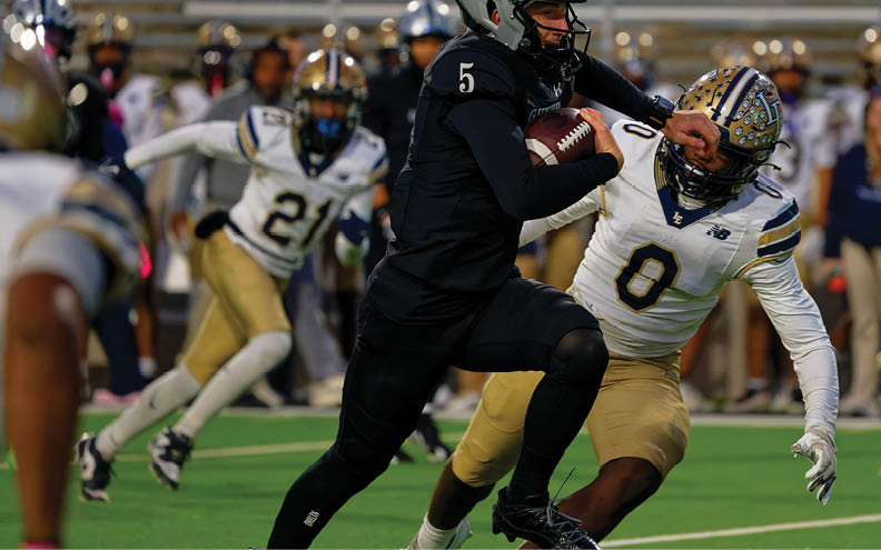Two people in sports uniforms are actively running on a green field during a game, with one wearing black and the other wearing white and gold. Description generated by AI