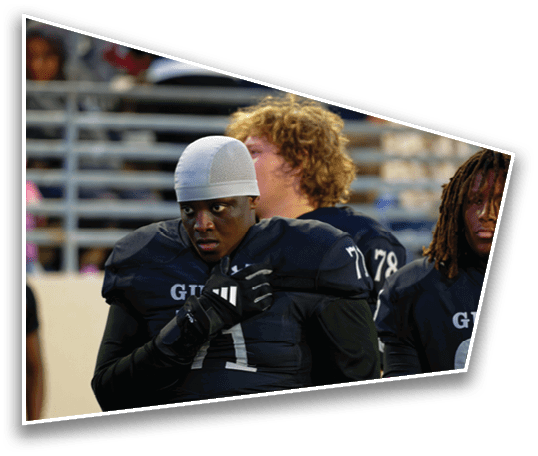 A person wearing a football uniform and helmet liner stands on a field with other players in the background. Description generated by AI