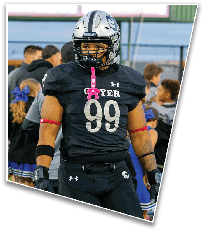 A person wearing a black football uniform with the number 99 and a helmet stands on a field with cheerleaders and other people in the background. Description generated by AI