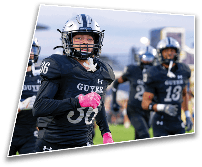 A person wearing a black football uniform with the number 36 and pink gloves is on a football field with other players in the background. Description generated by AI