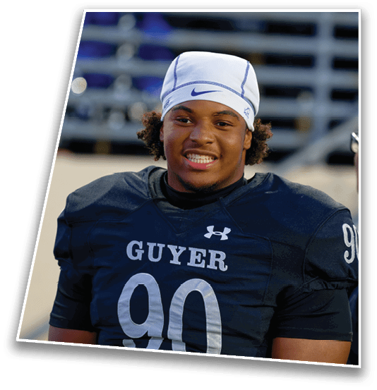 A person wearing a football uniform with the number 90 and the word Guyer on the jersey is smiling while standing in a stadium. Description generated by AI