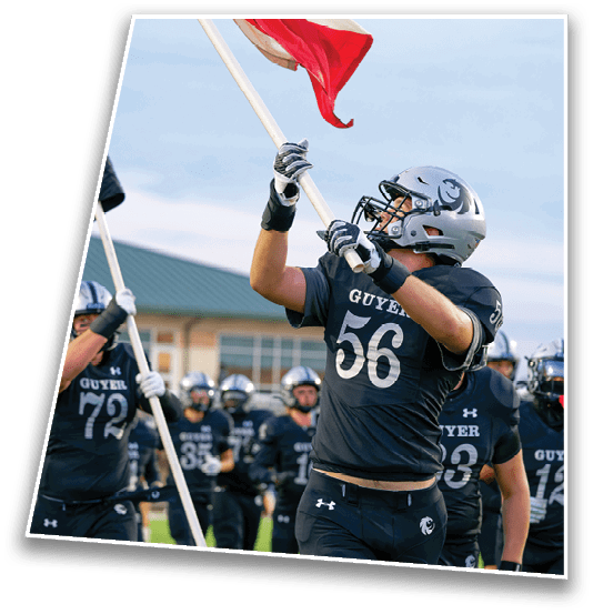 People in football uniforms are holding flags and appear to be celebrating or rallying on a field with a building in the background. Description generated by AI
