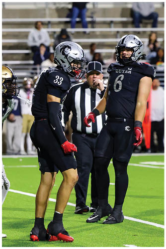 Three people in football uniforms and a referee stand on a field with a football on the ground near them during a game. Description generated by AI