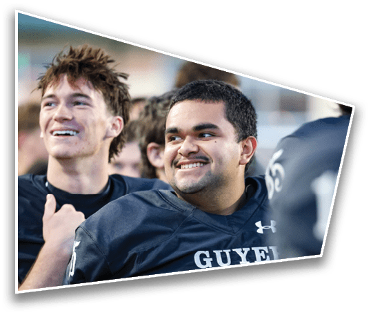People wearing football uniforms are smiling and standing close together, appearing to celebrate or enjoy a moment during a game or practice. Description generated by AI