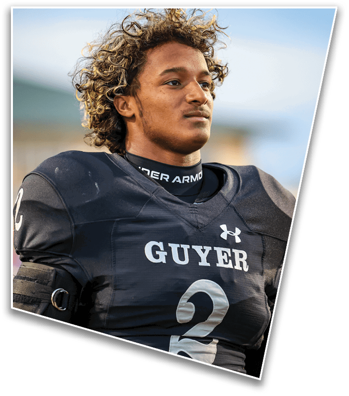 A person with curly hair wearing a black football uniform with the word “GUYER" and the number 2 on the front is looking off into the distance. Description generated by AI