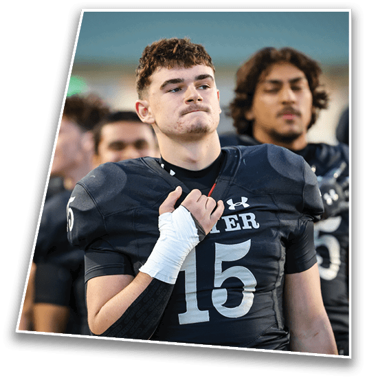 A person with short curly hair and a serious expression is in the foreground wearing a dark sports jersey, with another person with longer hair blurred in the background. Description generated by AI