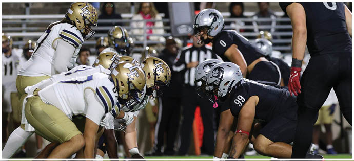Two opposing American football teams are lined up at the line of scrimmage on a green field, ready for the play to start. Description generated by AI