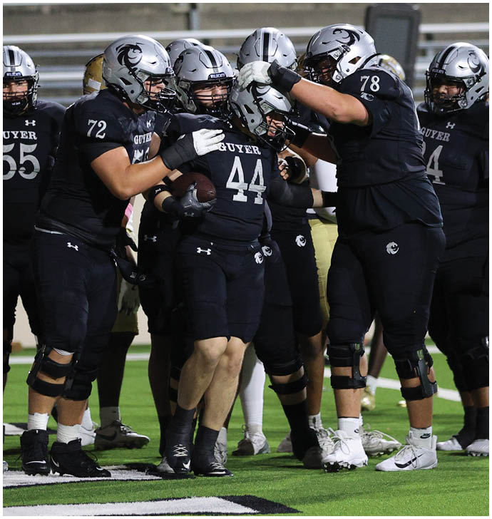 A group of football players in black uniforms and helmets are celebrating on a field, with one player holding a football. Description generated by AI